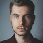 Close-up portrait of a young man with facial hair and a serious expression.